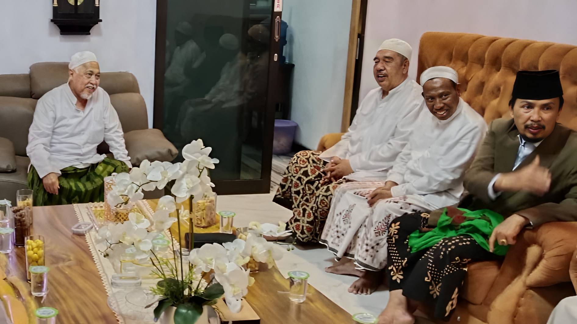 KH. A. Fuad Nur Hasan duduk bersama pengurus Jatma Aswaja Jawa Timur di ruang tamu Pondok Pesantren Sidogiri, mengenakan busana putih dan sarung, dalam suasana silaturahmi yang hangat dan akrab.