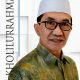 KH. Kholilurrahman, Bupati Pamekasan periode 2025–2030, mengenakan peci putih dan batik hijau, berpose dengan latar modern dan namanya tertulis vertikal.