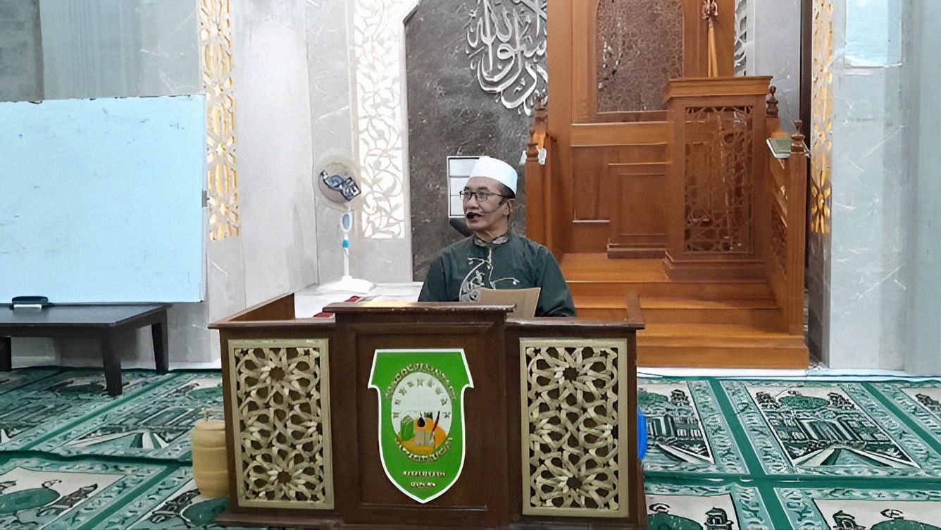 KH. Kholilurrahman memberi kajian kitab kuning di depan mimbar masjid pesantren dengan menggunakan mikrofon headset dan duduk di balik meja mimbar kayu berlogo Ponpes Matsaratul Huda.