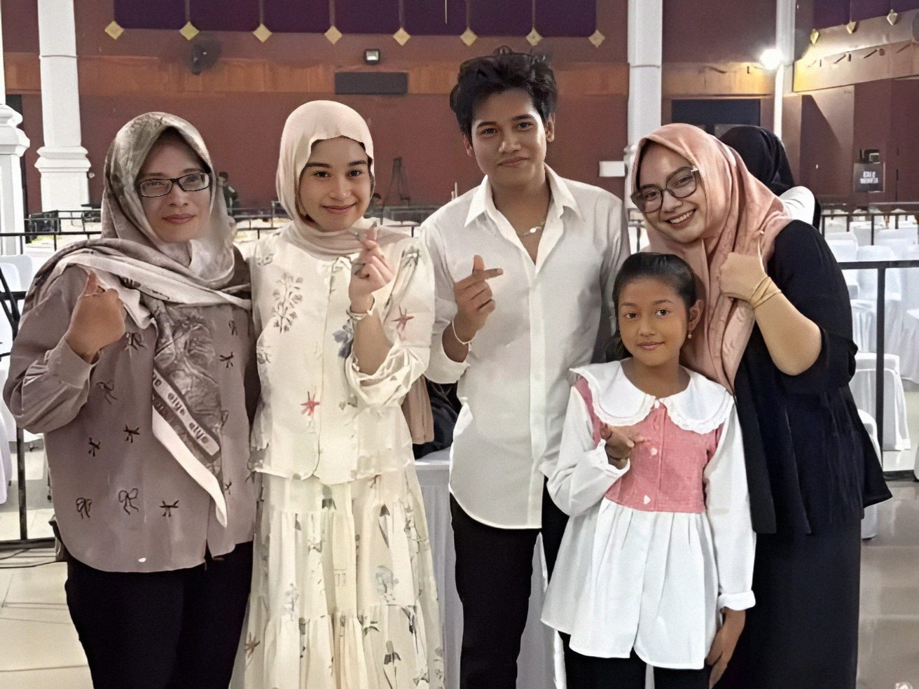 Seorang penyanyi pria berfoto bersama empat perempuan dari berbagai usia di dalam gedung acara dengan suasana formal.