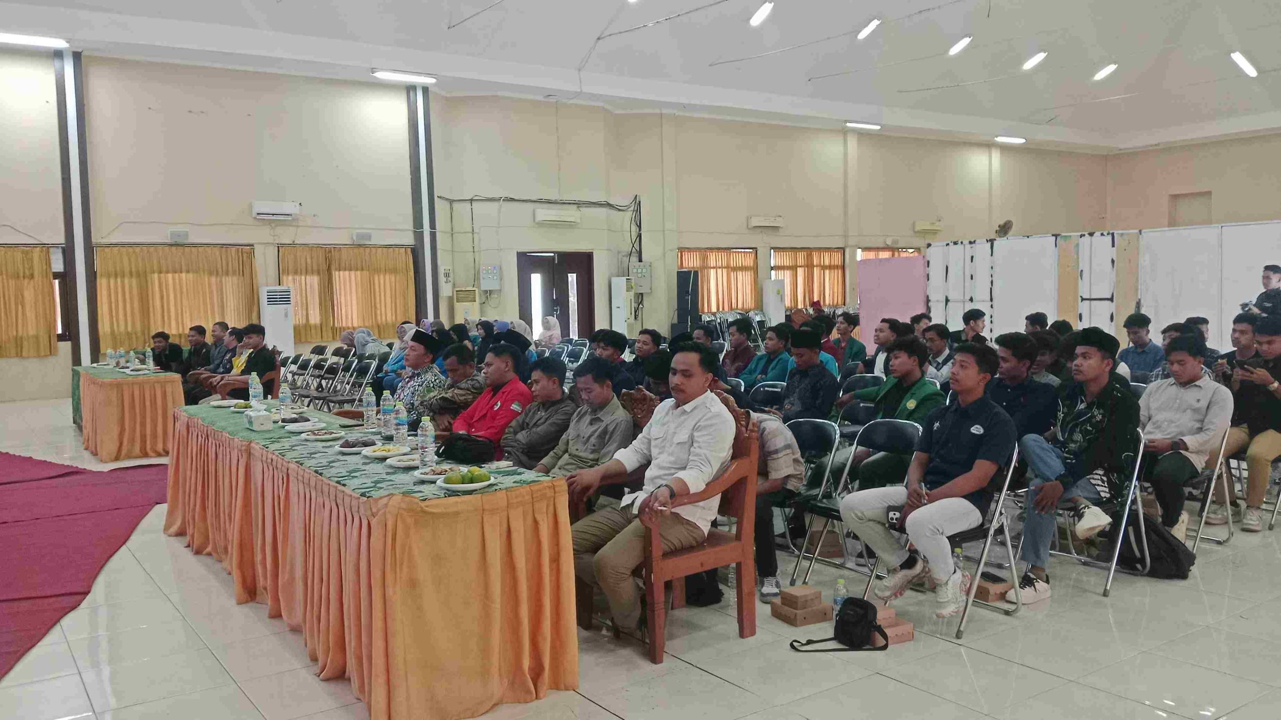 Suasana peserta RAPIMDA BEM Nusantara Jatim duduk di kursi auditorium pusat mengikuti acara dengan meja tamu undangan di bagian depan.