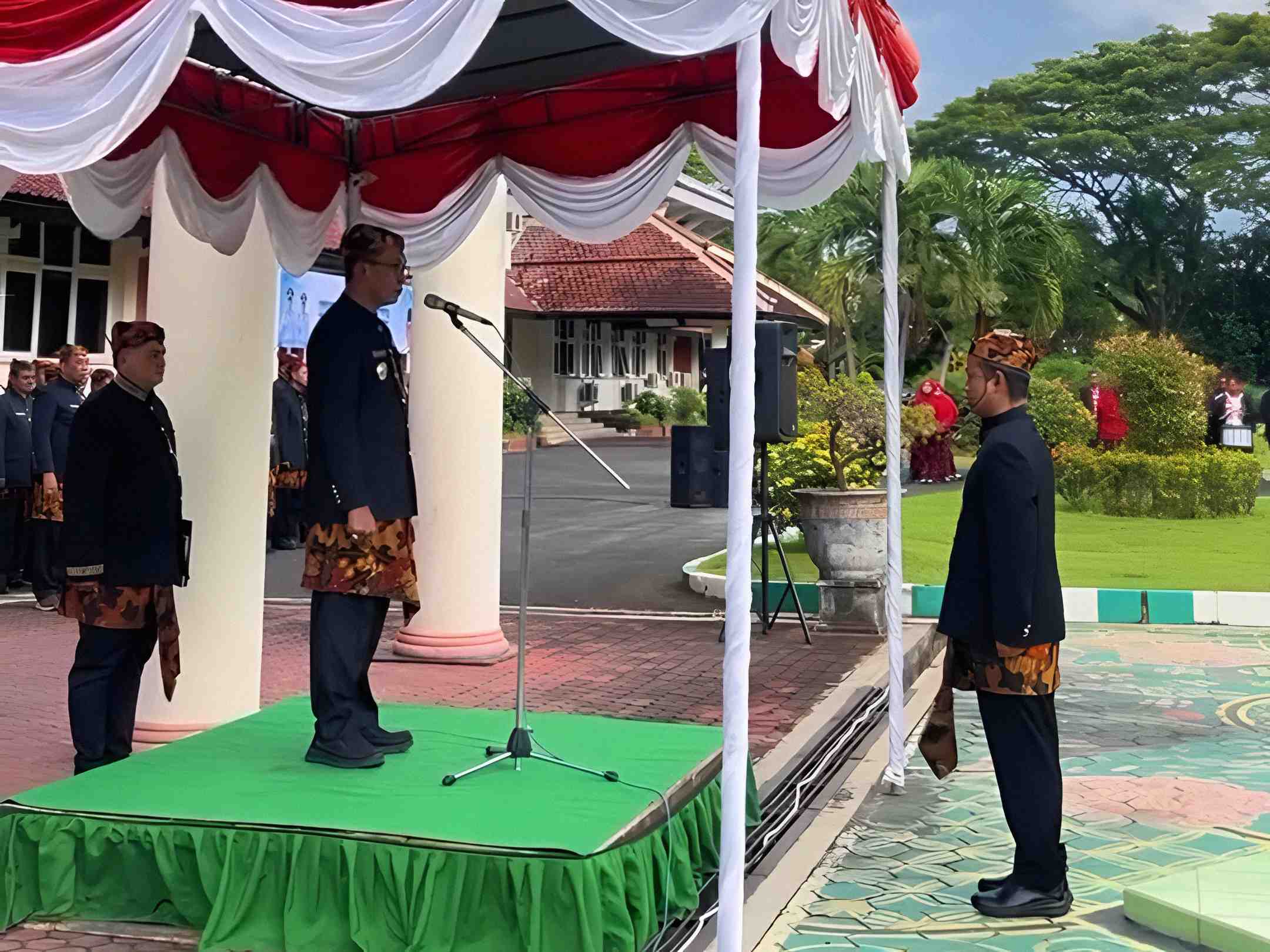 Bupati Pamekasan memimpin upacara Hardiknas 2026 di podium dengan peserta mengenakan pakaian adat di halaman kantor bupati.