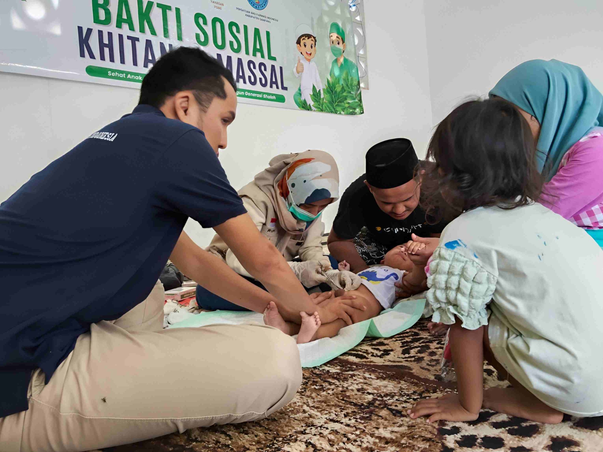 Tenaga kesehatan melakukan khitan kepada seorang anak dalam kegiatan Bakti Sosial Khitanan Massal, didampingi petugas dan keluarga.