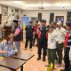 Petugas gabungan memeriksa sebuah ruangan bersama perempuan yang sedang membaca dokumen.