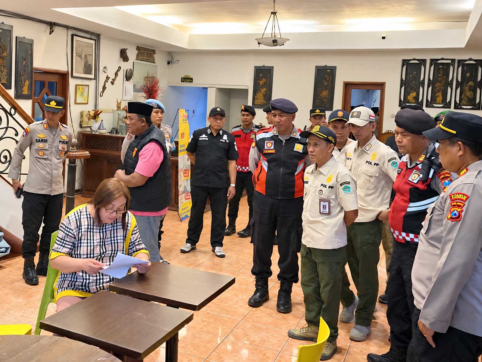 Petugas gabungan memeriksa sebuah ruangan bersama perempuan yang sedang membaca dokumen.