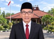 Bupati Pamekasan Kholilurrahman mengenakan jas dan peci dengan latar Pendopo Ronggosukowati.
